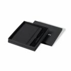 Black notebook and pen set in an open black gift box with the lid beside it.