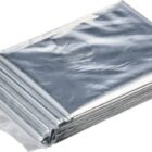 A folded, shiny silver emergency blanket is shown, reflecting light. It is neatly packed in a transparent plastic cover, emphasizing its compact and portable design.