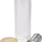 A clear glass travel tumbler with a cylindrical shape is displayed. It is accompanied by a bamboo lid and a stainless steel infuser lying beside it. The tumbler is open and empty.