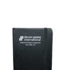 Close-up of a black notebook with devon-peake international professional freight management and a phone number printed on the cover in white. An elastic band is wrapped around the notebook.
