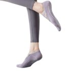Close-up of a persons lower legs wearing gray leggings and gray non-slip socks with white grips on the soles. The person is posed with one leg slightly bent in front of the other as if stretching or balancing.