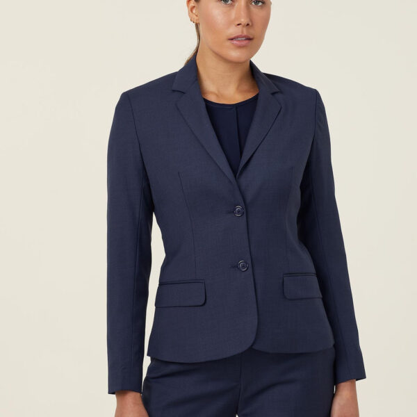 A person wearing a fitted navy blue suit with a blazer and matching pants stands against a plain light background. The blazer has two buttons and flap pockets. The person has long hair tied back and appears to be looking towards the camera.