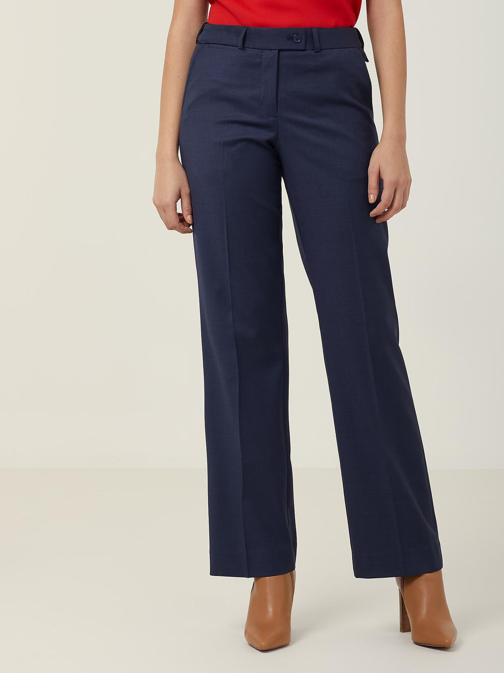 A person wearing high-waisted navy blue trousers and a red top. The pants have a tailored fit with flared legs. Brown heeled shoes complete the outfit. The background is plain light gray.