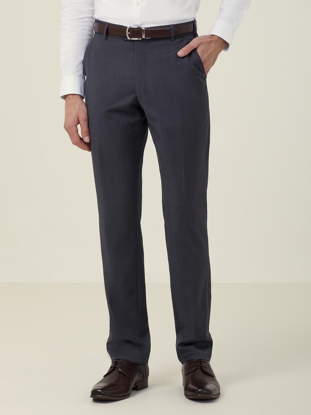 A person is wearing dark gray dress pants, a white long-sleeved shirt, and brown dress shoes. Their left hand is in their pocket, and they have a black belt. The background is plain off-white.