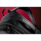 Close-up of a black backpack with elleven logo on a strap, against a red background.
