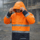 Person in Rainguard Flame-Resistant Outerwears adjusts hood while standing in the rain.