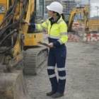 Woman in Queentech Women's Flexguard Pro Motion Pants inspects excavator with clipboard.