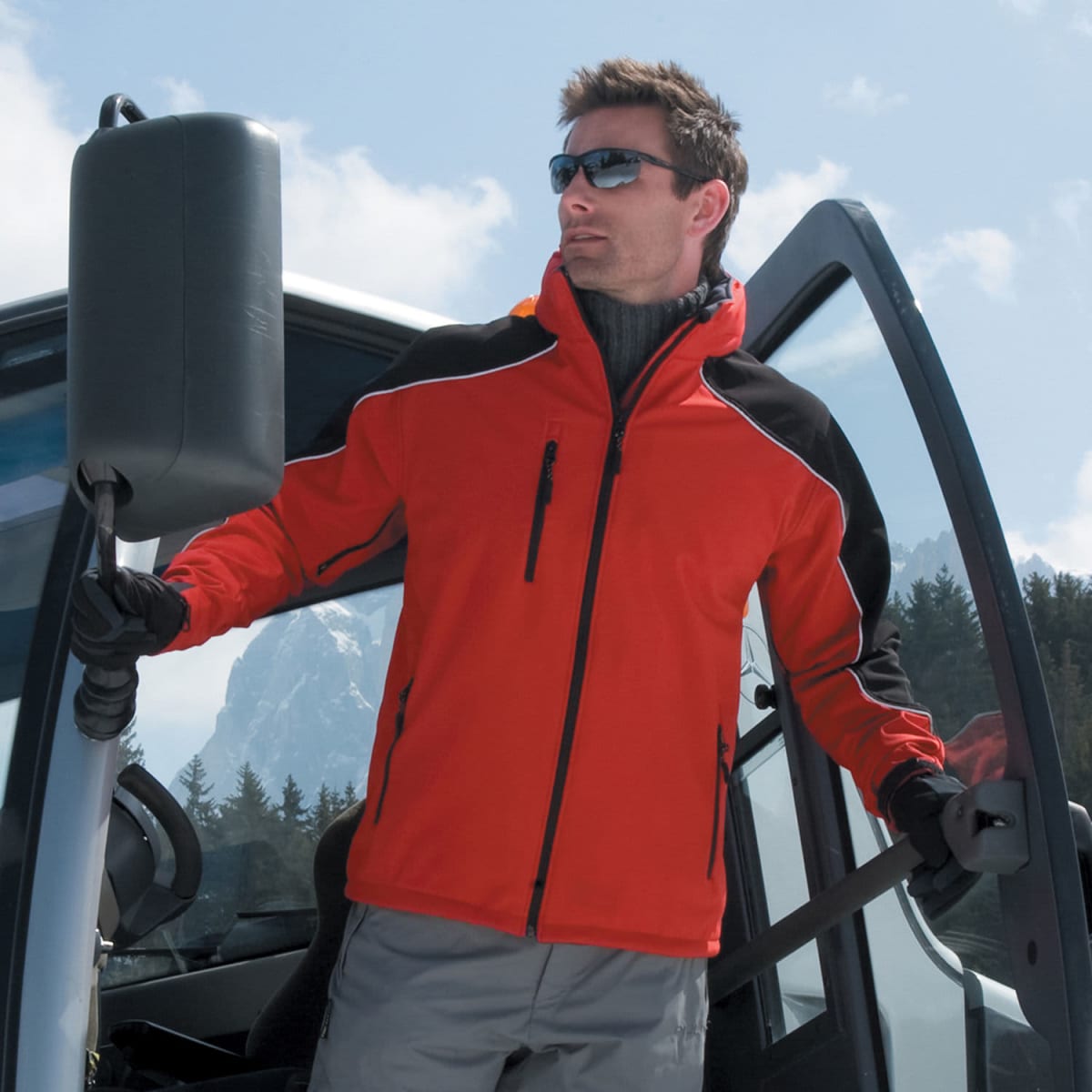 Man in red jacket and sunglasses holds kayak paddle beside open car door outdoors.