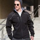 Man in sunglasses and beanie wearing a black jacket, standing on outdoor steps.