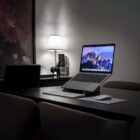 A laptop on a stand with a keyboard and mouse on a desk in a dimly lit room.