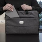 Person placing a gray tablet into a front pocket of a gray laptop bag on a table.