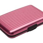 A small, rectangular, pink metallic hard case with a black clasp and ribbed texture.