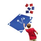 A child in a red shirt tosses a bean bag towards a blue target board on the ground with a hole in the center. The board has the word Aegis printed on it. Several red and blue bean bags are scattered in the air.