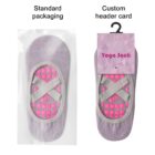 Two yoga socks with pink grips and crisscross straps in grey. The left sock is in standard packaging, while the right sock features custom packaging with a Yoga Sock header card on a hanger.