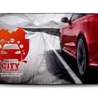 Red sports car driving on a road with City Car Wash logo and text on left side.