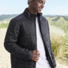 Man in a gray beanie and black puffer jacket standing outdoors, smiling.