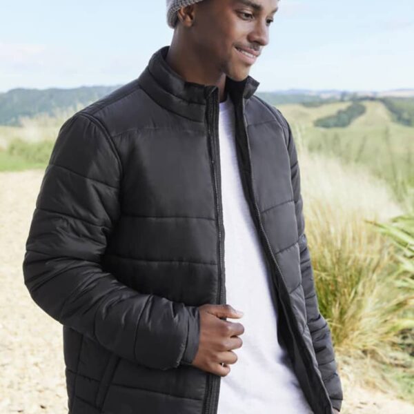 Man wearing a gray beanie and black puffer jacket standing outdoors and smiling.