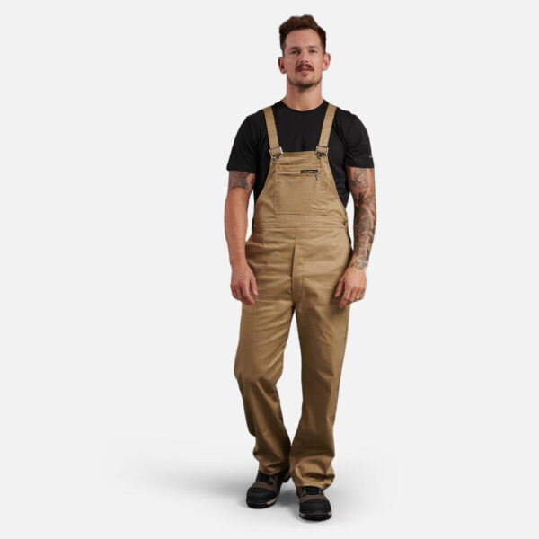 Man in tan overalls and black t-shirt styled with Explorer Shield, against white background.