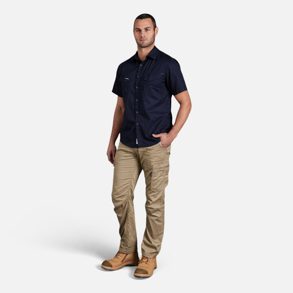 Man in a dark Explorer Shield shirt with tan cargo pants and boots, standing casually.