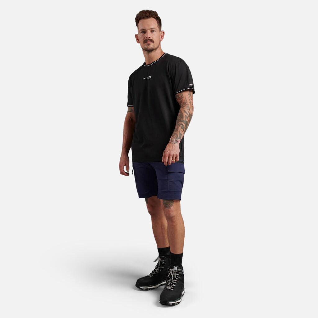 Man in black t-shirt, navy shorts, and Explorer Shield shoes stands against a white background.