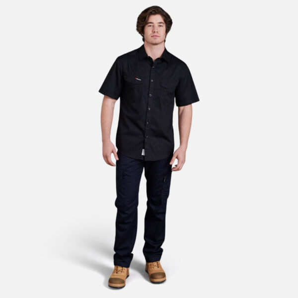 Man wearing black Explorer Shield tee, dark pants, and tan boots, facing forward.