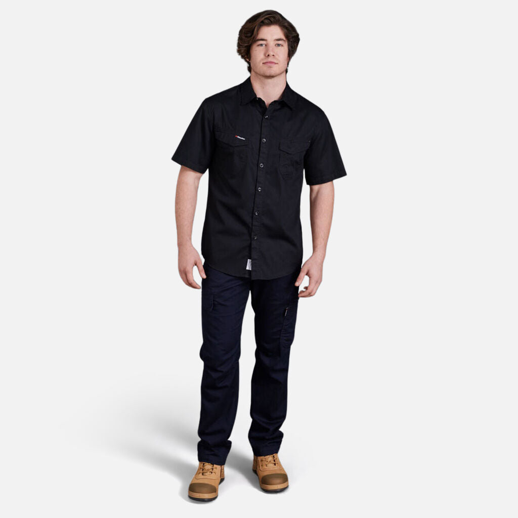 Man wearing black Explorer Shield tee, dark pants, and tan boots, facing forward.