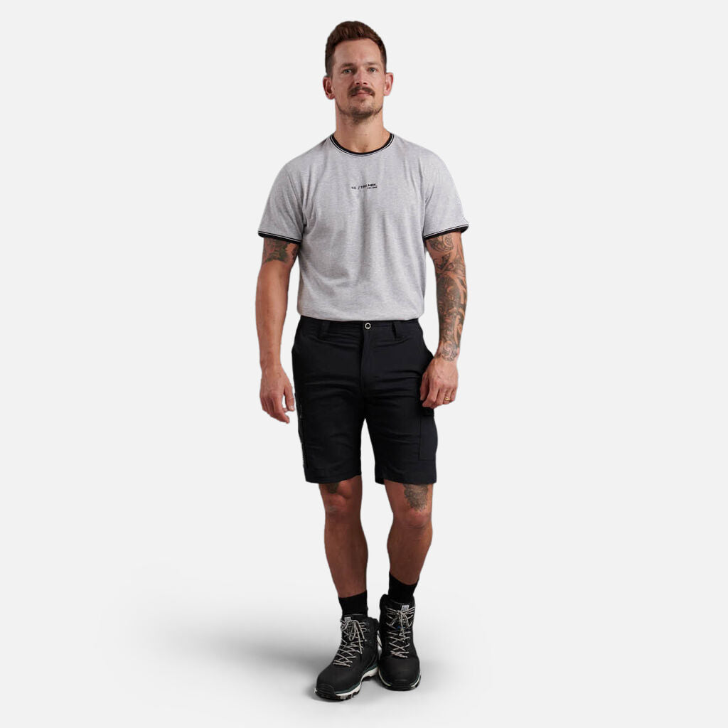 Man in an Explorer Shield gray t-shirt, black shorts, and boots against a white background.