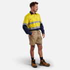 Man in Explorer Shield shirt, khaki shorts, and boots, hand in pocket.