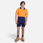 Man in Explorer Shield polo, navy shorts, and tan boots standing.