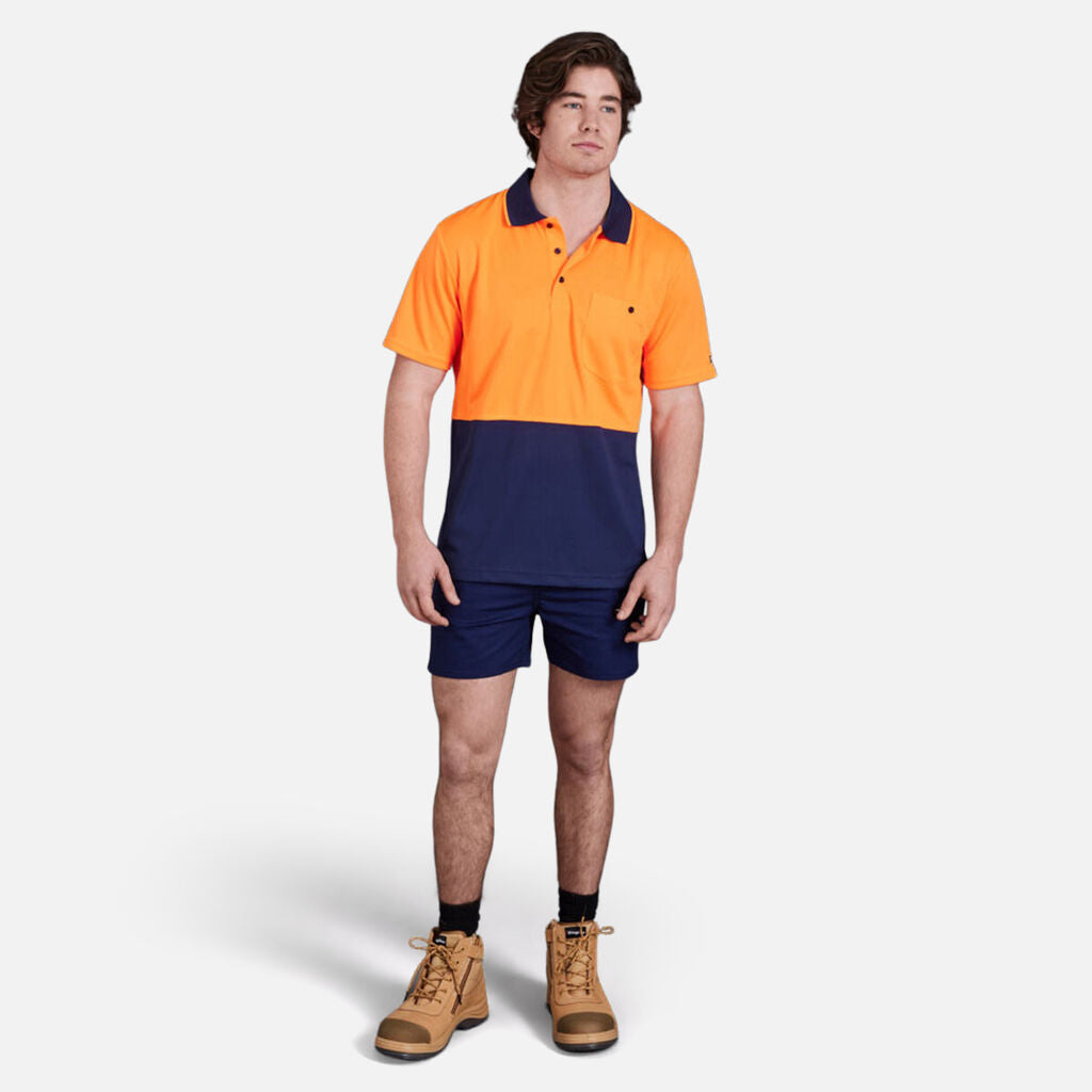 Man in Explorer Shield polo, navy shorts, and tan boots standing.
