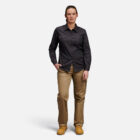 Woman in dark shirt, tan pants, brown boots with Explorer Shield stands against white background.