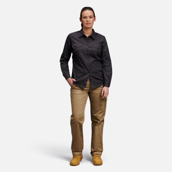 Woman in dark shirt, tan pants, brown boots with Explorer Shield stands against white background.