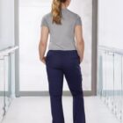 Person in a gray shirt and navy pants stands facing away in a bright hallway.