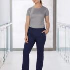 Woman in a gray t-shirt and navy pants standing in a bright hallway with glass railings.