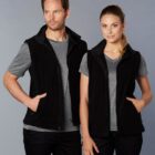 Man and woman wearing matching black vests over grey shirts, standing together, facing forward.