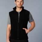 Man wearing a black sleeveless zip-up vest over a grey t-shirt, standing against grey backdrop.