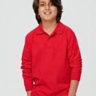 Smiling boy in a red long-sleeve polo shirt with hands in pockets, standing against a gray background.