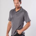 Man in a gray polo shirt with one hand in his pocket, standing against a plain background.