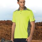 Man in a neon yellow work shirt holding a tool, standing in front of a dirt mound.