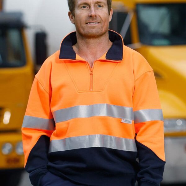 Man in a high-visibility orange jacket standing in front of yellow trucks.