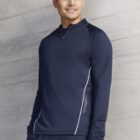 Man in navy blue athletic jacket standing against a light gray concrete wall, smiling.