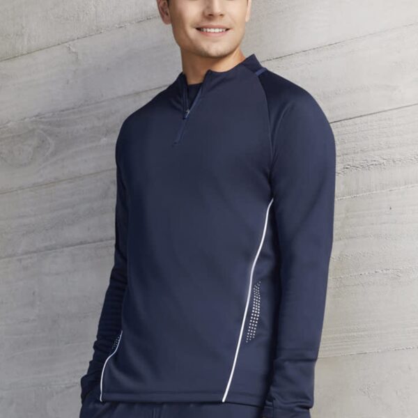 Man wearing a navy blue long-sleeve athletic shirt, standing and smiling against a gray wall.