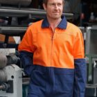 Man in orange and navy workwear stands near industrial machinery, looking to the side.