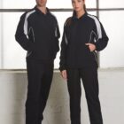 Two people in matching black and white tracksuits standing indoors.