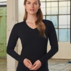 Woman in a black long-sleeve V-neck shirt standing indoors with folded hands.