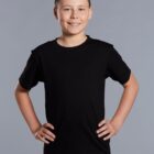 Smiling boy in a black t-shirt stands with hands on hips against a gray background.