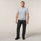 A man stands against a plain background, dressed in a light gray T-shirt, dark gray cargo pants, and black boots. In his hands, he gently holds an Emz A5 Notebook by his side while gazing slightly away.