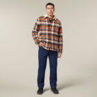 A man stands against a plain background holding an Emz A5 Notebook. Hes wearing a plaid flannel shirt with a shearling collar, blue pants, and black shoes. His short hair complements his casual pose with one hand in his pocket.