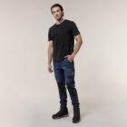 A man poses confidently against a simple backdrop, wearing a black t-shirt, dark blue cargo pants with black knee patches, and black boots. He holds an Emz A5 Notebook in his left hand while his right hand rests in his pocket.