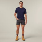 Against a plain background, someone casually flips through an Emz A5 Notebook with their right hand while wearing a dark blue T-shirt, gray shorts, and tan boots. Dark socks with orange stripes peek out, and their left hand rests in their pocket as they exude a relaxed expression.